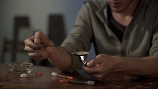 Ein Drögensichtiger erhitzt einen Heroinlöffel mti einem Feuerzeug.