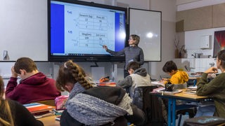 Eine Lehrerin steht vor einer Klasse an einem Whiteboard.