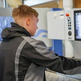 Ein junger Mann steht in Arbeitskleidung vor einem Bildschirm.