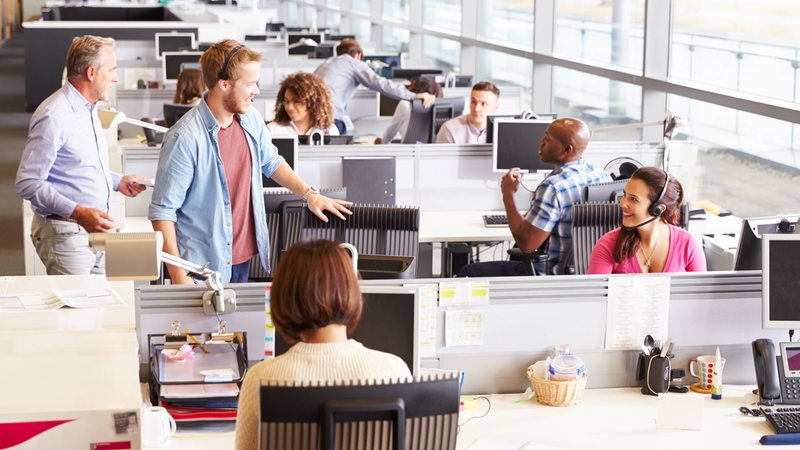 Mehrere Personen sitzen vor Computern, ein Mann kommt dazu.