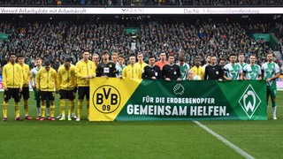 Die Spieler von Werder und Dortmund stellen sich vor dem Spiel hinter einem Banner mit der Aufschrift "Für die Erdbebenopfer – Gemeinsam helfen" auf.