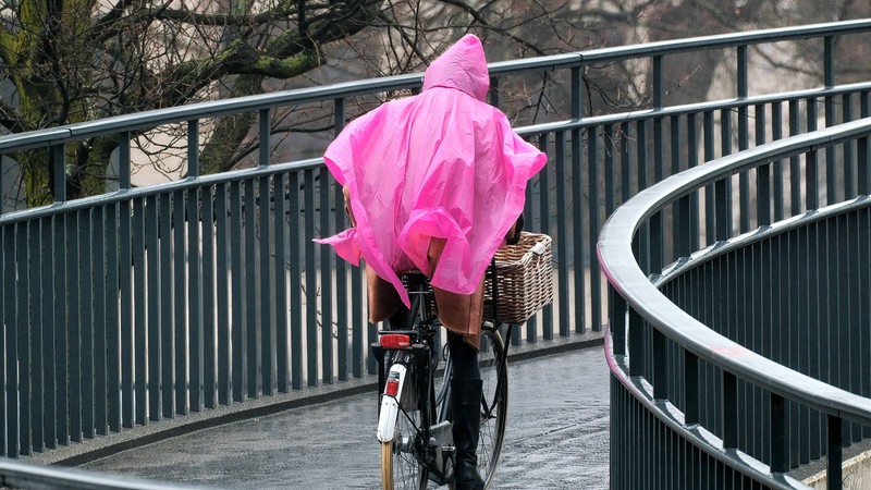 Mensch fährt mit Rad mit pinkem Regenponcho