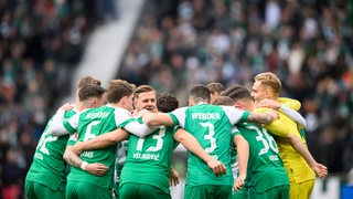 Werder-Spieler um Niclas Füllkrug stehen vor dem Spiel Arm in Arm im Kreis zusammen.