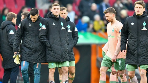 Enttäuschte Werder-Spieler stehen nach der Niederlage auf dem Rasen.
