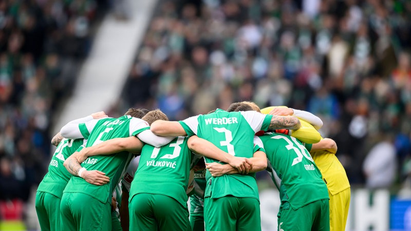 Die Fußballspieler des SV Werder Bremens stehen in einem engen Kreis zusammen und haben die Köpfe zusammengesteckt.