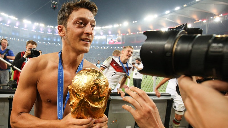 Fußballer Mesut Özil steht mit nacktem Oberkörper und dem goldenen WM-Pokal in der Hand im Stadion von Rio vor den Fotografen.