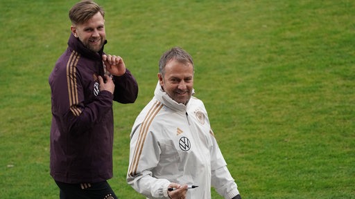 Werder-Stürmer Niclas Füllkrug geht lächelnd hinter Bundestrainer Hansi Flick am Rande des Trainings der Nationalmannschaft hinterher.