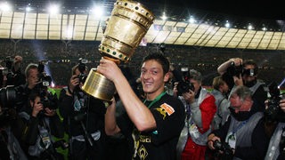 Mesut Özil hält strahlend und umringt von Fotografen den goldenen DFB-Pokal in die Höhe.