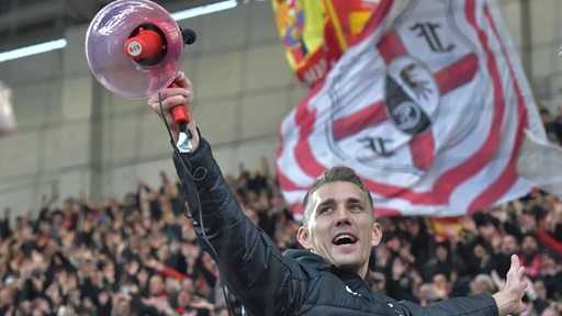 Fußball-Profi Nils Petersen steht strahlend mit einem Megafon in der Hand im Fan-Block des SC Freiburg.