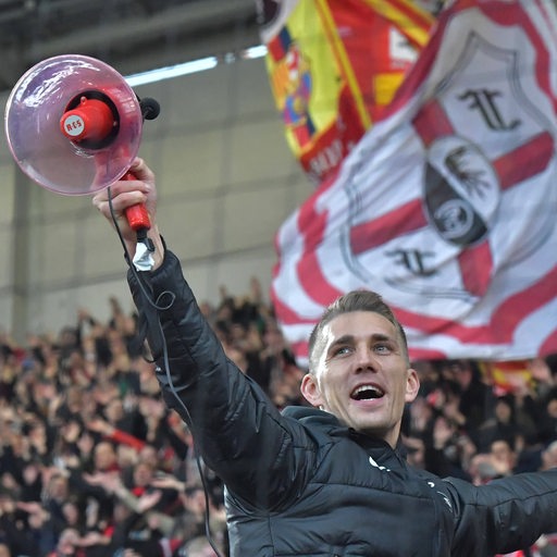 Fußball-Profi Nils Petersen steht strahlend mit einem Megafon in der Hand im Fan-Block des SC Freiburg.