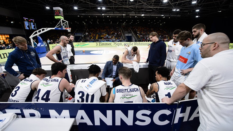 Die Basketball-Spieler der Eisbären Bremerhaven sitzen und stehen während einer Auszeit um Trainer Stephen Key herum.