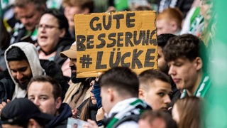 Ein Werder-Fan hält im Weser-Stadio ein Pappschild hoch mit der Aufschrift: "Gute Besserung Lücke".