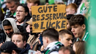 Ein Werder-Fan hält im Weser-Stadio ein Pappschild hoch mit der Aufschrift: "Gute Besserung Lücke".