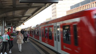 Fahrgäste schauen an einem Bahngleis einem einfahrenden Zug hinterher.