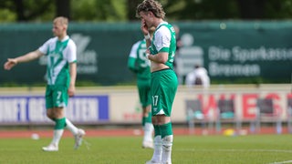 Werders U23-Spieler Ronan Kratt steht enttäuscht über die Niederlage gegen Hannover auf dem Feld und hält sich die Hand vors Gesicht.