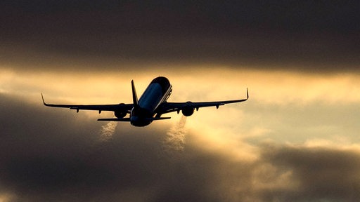 Ein Flugzeug startet während des Sonnenuntergangs, im Gegenlicht sind die Abgase gut zu erkennen.
