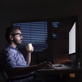 Ein Mann sitzt im Dunkeln an seinem Schreibtisch und arbeitet.