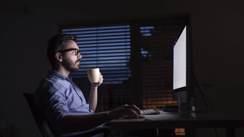 Ein Mann sitzt im Dunkeln an seinem Schreibtisch und arbeitet.