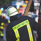 Ein Feuerwehrmann holt bei einem Einsatz einen Feuerwehrschlauch aus dem Wagen. (Symbolbild)