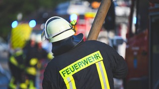 Ein Feuerwehrmann holt bei einem Einsatz einen Feuerwehrschlauch aus dem Wagen