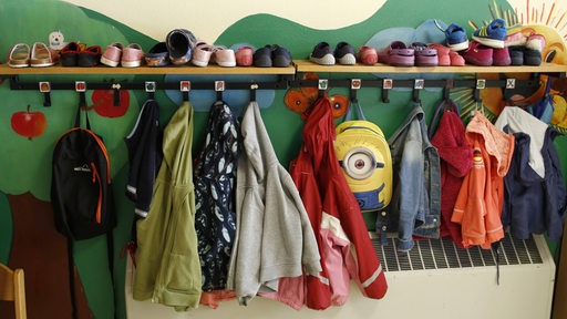 Jacken von Kindern hängen an Kleiderhaken in einem Kindergarten.