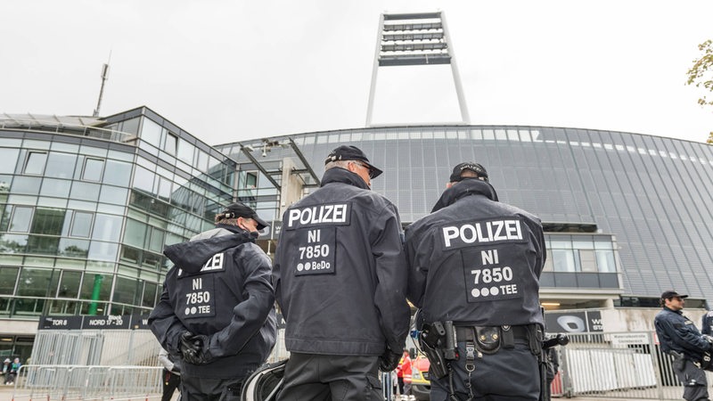 Drei Polizisten stehen mit dem Rücken zur Kamera vor dem Weser-Stadion.