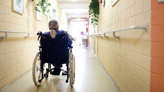 Alte Frau im Rollstuhl auf dem Flur eines Altenpflegeheims. (Archivbild)