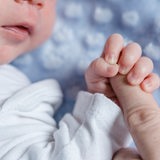 Ein Baby umfasst einen Finger (Symbolbild)