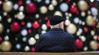 Ein Mann sitzt allein auf einer Bank vor einem geschmückten Weihnachtsbaum (Symbolbild)