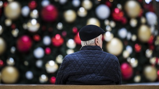 Ein Mann sitzt allein auf einer Bank vor einem geschmückten Weihnachtsbaum (Symbolbild)