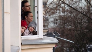 Eine Familie mit Kindern schaut aus dem Fenster ihrer Wohnung (Symbolbild)
