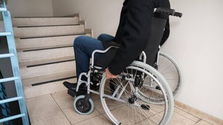 Ein Mann im Rollstuhl steht vor für ihn unüberwindbaren Treppen.