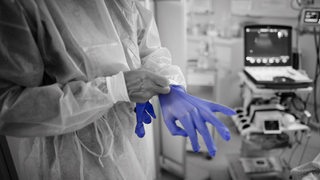 Eine Ärztin zieht sich blaue Handschuhe in einer Intensivstation an.