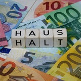 Auf Euronoten liegende Würfel zeigen das Wort "Haushalt" (Symbolbild)