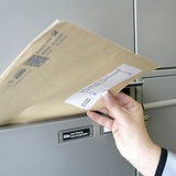 Postbotin steckt einen Brief in einen Briefkasten.
