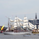 Mehrere Schiffe fahren durch den Hafen in Bremerhaven. Im Hintergrund sind Gebäude und viele Menschen zu sehen.