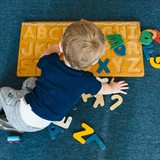 Ein Kind im Kindergarten spielt mit einem Buchstaben-Puzzle.