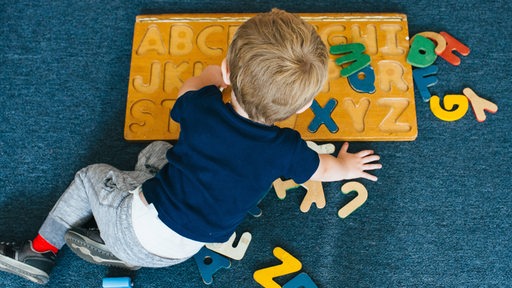 Ein Kind im Kindergarten spielt mit einem Buchstaben-Puzzle.