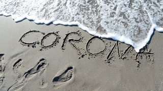 Das Wort "Corona" ist in den nassen Sand eines Strandes geschrieben (Symbolfoto)
