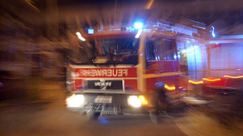 Ein Feuerwehrwagen fährt nachts mit Blaulicht zu einem Einsatz.