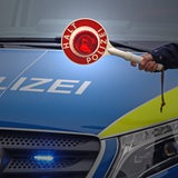 Eine Hand hält eine Polizeikelle vor ein Polizeiauto.