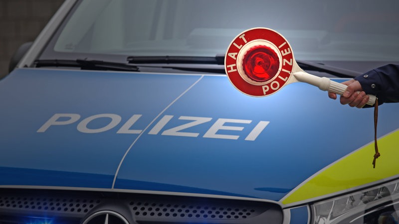Eine Hand hält eine Polizeikelle vor ein Polizeiauto.