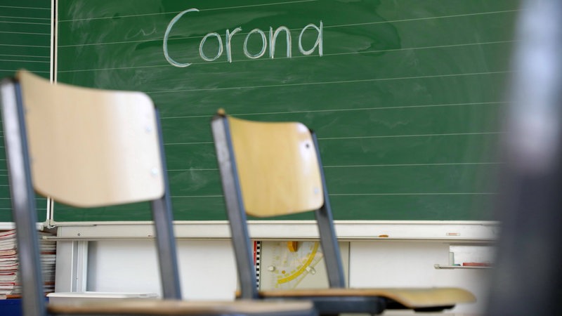 Stühle auf dem Tisch - leeres Klassenzimmer der 2. Klasse einer Grundschule, an der Tafel steht das Wort Corona. (Symbolbild)