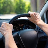 Die Hände einer Seniorin am Lenkrad eines Autos 