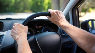 Die Hände einer Seniorin am Lenkrad eines Autos 