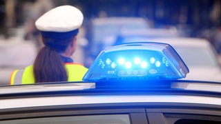 Polizistin steht vor einem Streifenwagen mit eingeschaltetem Blaulicht