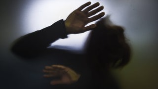 Eine nicht erkennbare Person mit langen Haaren hält ihre Hände schützend vor ihr Gesicht.