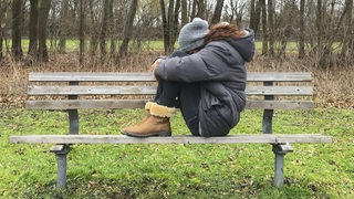 Junge Frau traurig und enttäuscht auf einer Parkbank im Wald sitzend.
