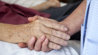 Die Hand einer Pflegerin hält die Hand eines sterbenden Mannes. (Symbolbild)
