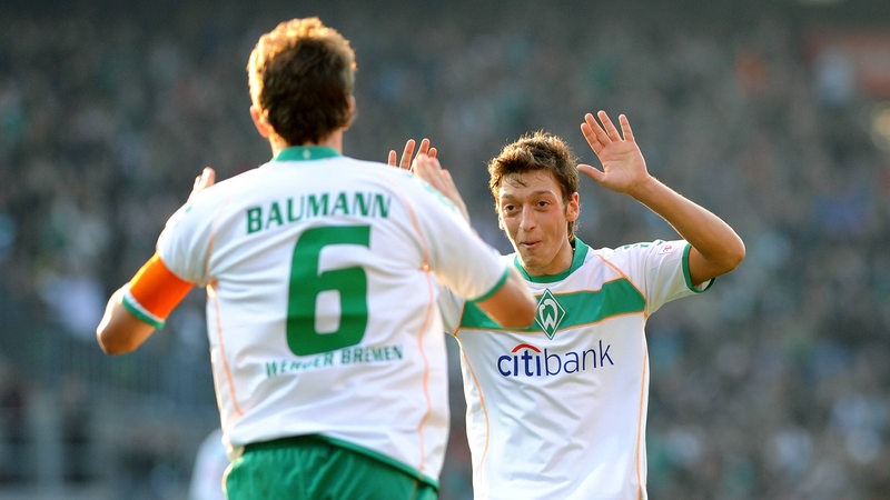 Frank Baumann und Mesut Özil klatschen auf dem Platz miteinander ab.